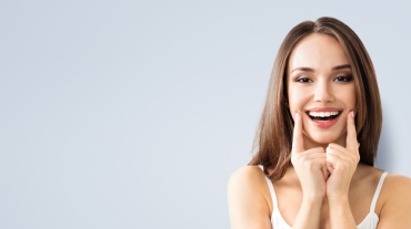 Young woman showing smile, in white casual smart clothing, on grey background, with copyspace area for advertisiment, text or slogan. Advertising concept. Horizontal banner composition.